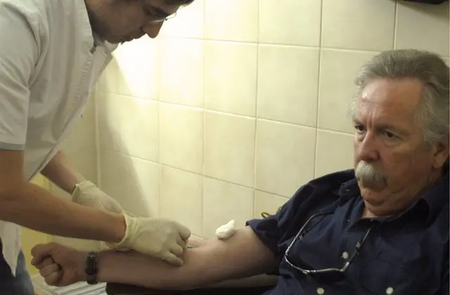 Enfermero le extrae la sangre a un paciente dentro de un cuarto de hospital.