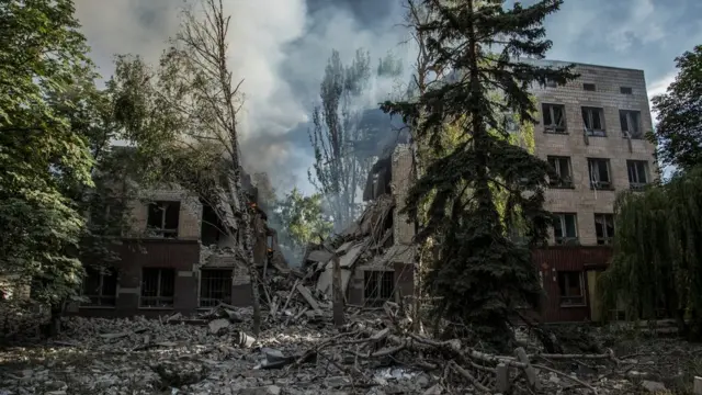 Smoke rises over remains of a building destroyed by a military strike in Lysychansk