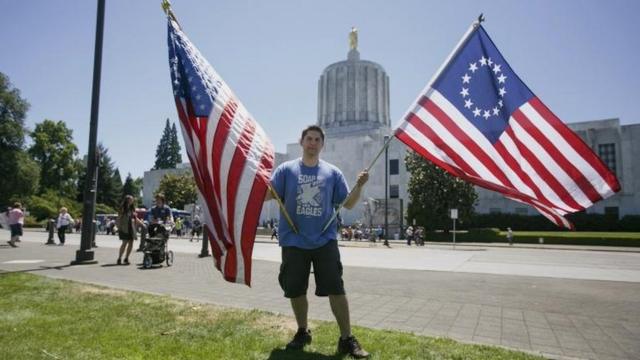 Un joven sostiene dos tipos de banderas de EE.UU.