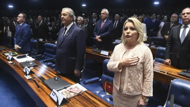 Selma Arruda aparece com a mão no peito, enquanto é executado o Hino Nacional, ao ladocasa das apostas futeboloutros parlamentares enfileirados