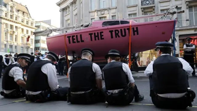 Полицейские силят рядом с розовым катером, который протестующие установили на перекрестке. На борту написано: "Скажите правду"