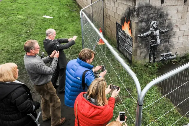 People gather around fences that have been erected to protect the latest piece of artwork by guerrilla artist Banksy on 20 December 2018
