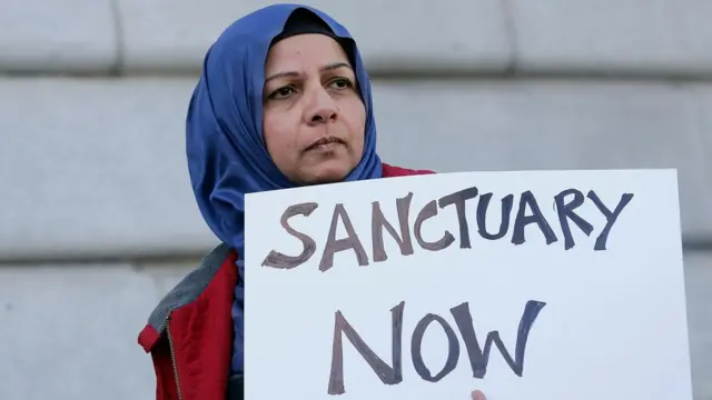 Una mujer musulmana sostiene un cartel que dice "Santuarios ahora".
