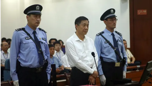 22 August 2013. Former Politburo member and Chongqing city party leader Bo Xilai, centre, on trial in eastern China's Shandong province. Standing flanked by security officers.