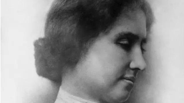 A black and white photo of Helen Keller's side profile. She has brown hair in a low bun and her eyes are downcast