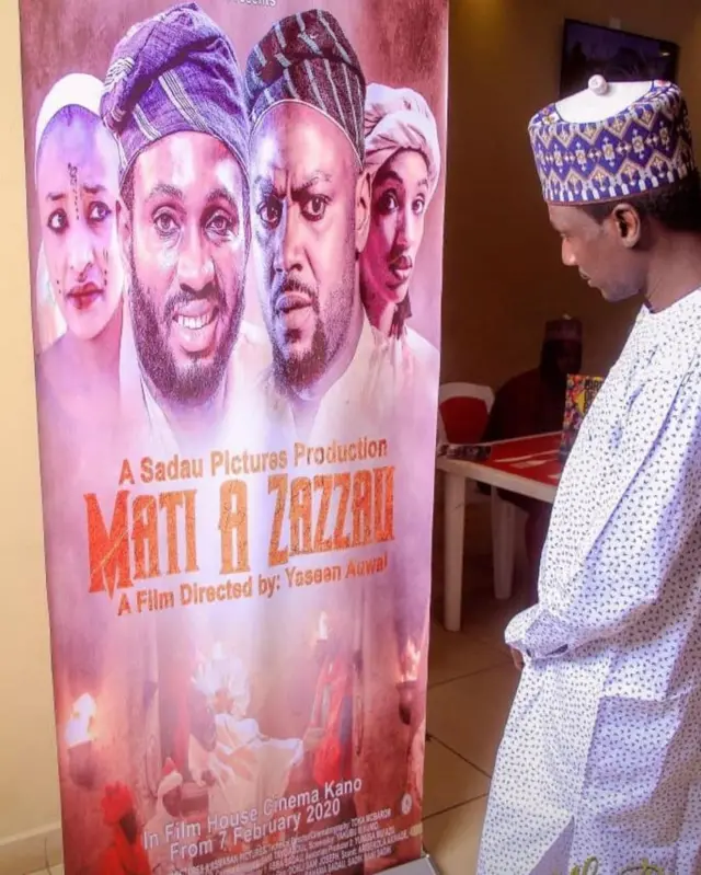 Wani matashi a gaban fostar fim din Mati a Zazzau wadda aka ajiye a kofar sinima ta Filmhouse da ke Kano. Za a soma nuna fim din ranar balwai ga watana Fabrairu.