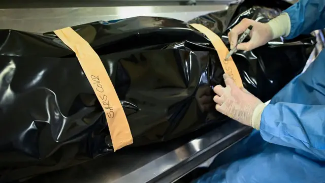 Патолог рядом с черным мешком с телом умершего от Covid-19 пациента