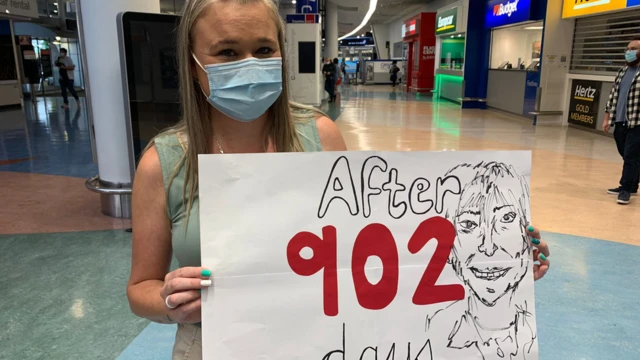 A woman carries a sign reading "After 902 days" at Auckland Airport