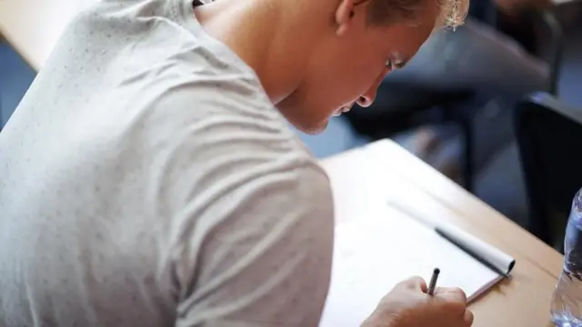 Un joven respondiendo a un examen en un pupitre