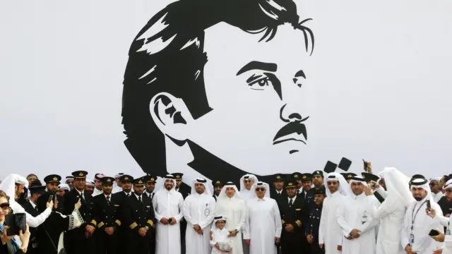 موظفو الخطوط الجوية القطرية أمام صورة الشيخ تميم