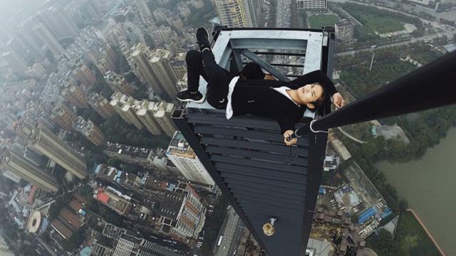 Wu Yongning uses a selfie stick to photograph himself reclining on top of a structure far above the surrounding buildings