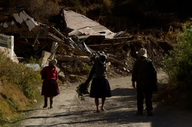 Tres personas caminando hacia la posta destruida.