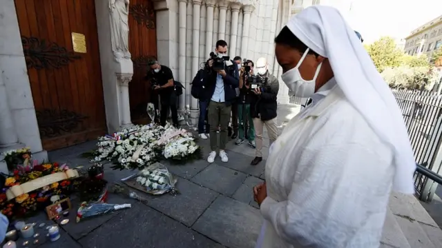A nun prays in front of candles and flowers left in tribute to the victims of a knife attack at the Notre Dame church in Nice, France, October 30, 2020