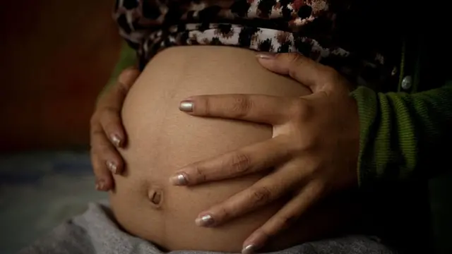 Teenage mum holds pregnant stomach.