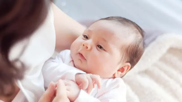 Um recém-nascido segurado nos braços da mãe parecendo contente