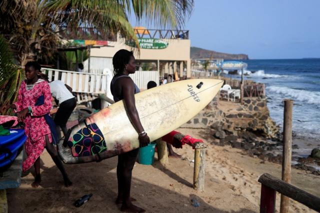 Khadjou Sambe se tient sur la plage avec sa planche de surf et regarde la mer