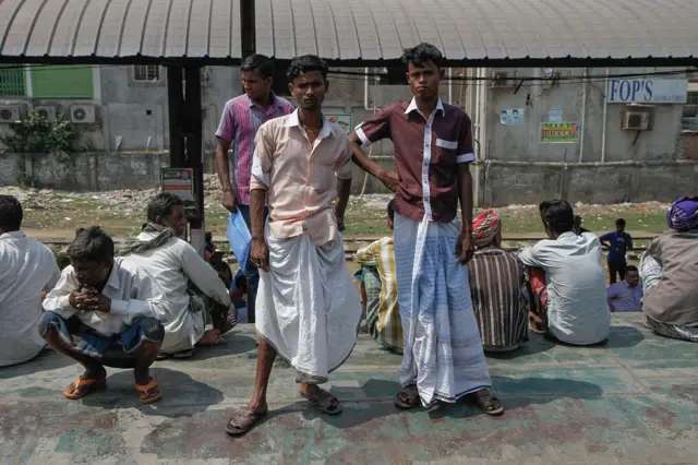 Krovovi susedne kompozicije koja se kreće prema Daki puna je ljudi. Većina muškaraca u Bangladešu, kao i indijskoj državi Zapadni Bengal i susednom Mjanmaru umesto pantalona nosi lungije, vrstu saronga karakterističnu za ovaj deo južne Azije.
