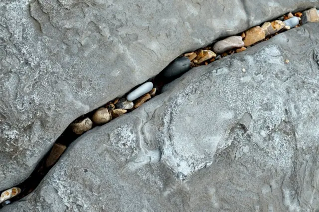 Smaller pebbles and stones sit in between the cracks of larger rocks