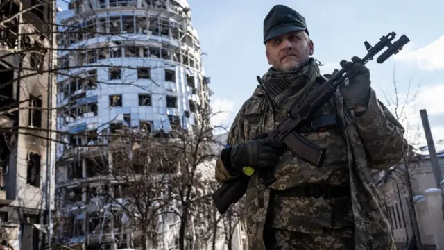 Umusirikare uhagaze imbere y'inyubako yangijwe na misile zayirashweho muri Kharkiv