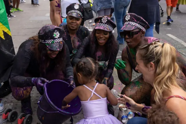 Участники карнавала в костюме полицейских угощают девочку конфетами