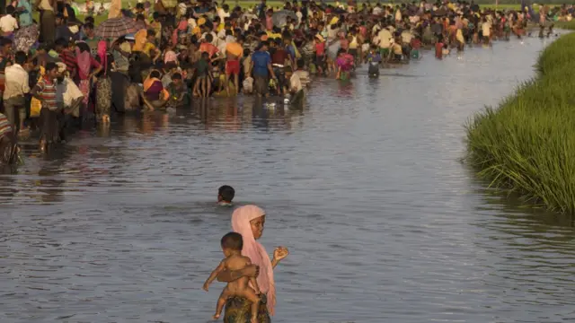 बच्चा लेकर नदी पार करती रोहिंग्या महिला