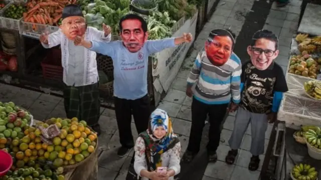 Seorang perempuan berfoto bersama warga yang mengenakan topeng pasangan Capres-Cawapres Joko Widodo-Ma'ruf Amin dan Prabowo Subianto-Sandiaga Uno dalam aksi di Pasar Gede, Solo, Jawa Tengah, Jumat (10/8). Aksi tersebut berharap pilpres 2019 berjalan dengan aman dan damai.