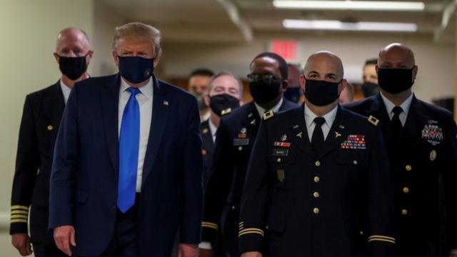 Trump e militares de máscara caminham em corredor de hospital