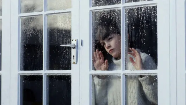 Dečak posmatra kišni dan kroz prozor