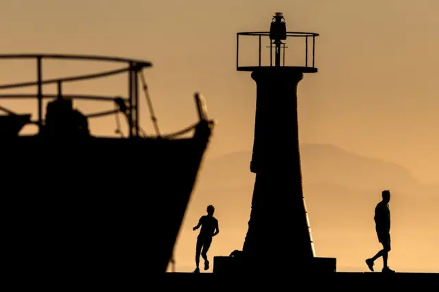 Masu gudun motsa jini suna sassarfa a Kalk Bay harbour wall a birnin Cape Town da ke Afirka ta gudu a ranar Alhamis