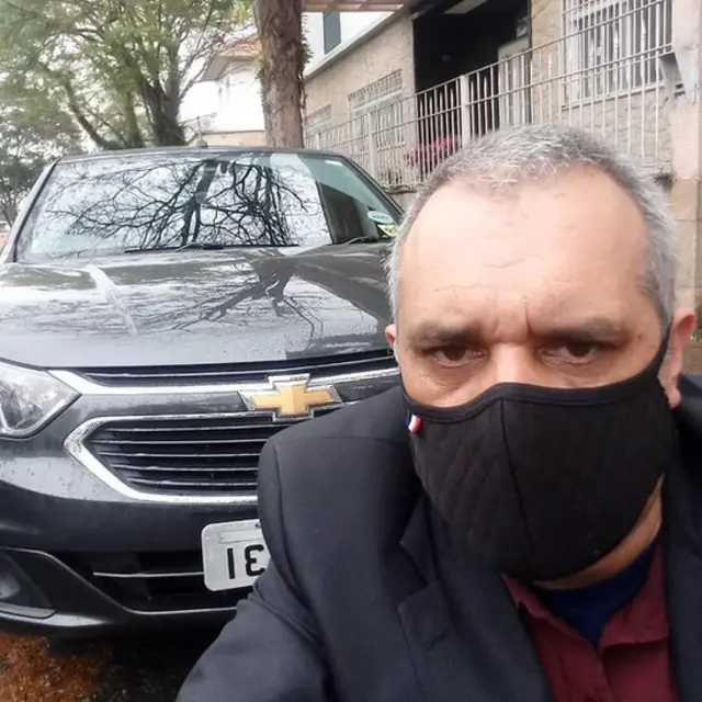 De máscara, Rosemar na frente do carro que usa para trabalhar como motoristacomo colocar dinheiro no esporte da sorteaplicativo