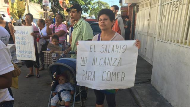 Pessoas fazem manifestação em rua da Venezuela. Entre elas, mulheres seguram cartazes em que se lê "sem água, sem luz, sem gás, sem transporte, sem dinheiro" e o salário não dá nem para comida"