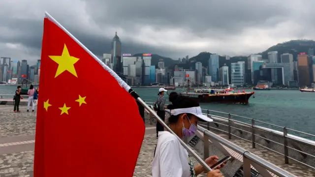 香港九龍尖沙咀碼頭觀景平台上一名參與中共建黨百年暨香港政權移交24週年活動的女子舉著中國國旗(1/7/2021)