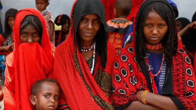 A woman, two young women and a child stare into the camera. They are wearing matching red.