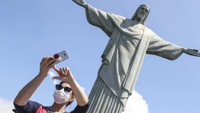 Pessoa com máscara tira foto no Cristo Redentor