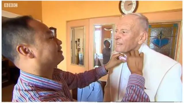 captura de pantalla de George Montague cuando su pareja le acomoda la corbata.