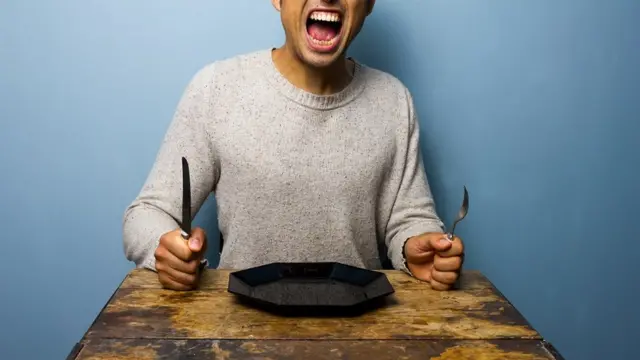 Hungry man sits at a table with plate, knife and fork Ọkunrin kan ti ebi n pa joko si ori tabili pẹlu sibi àti