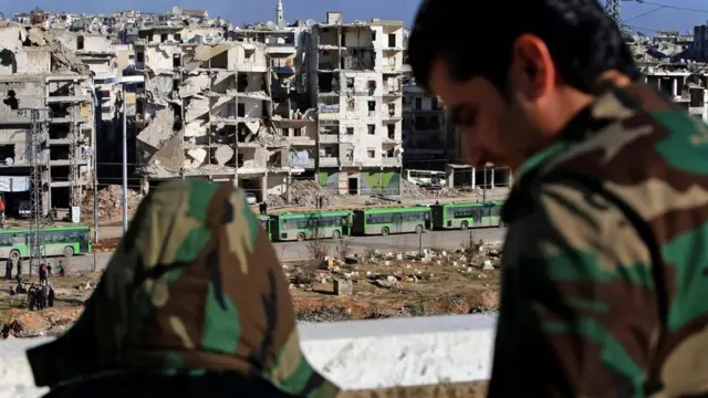 یکی از نیروهای وفادار به بشار اسد شاهد خروج اتوبوس‌ها از شرق حلب است. ۱۵ دسامبر ۲۰۱۶