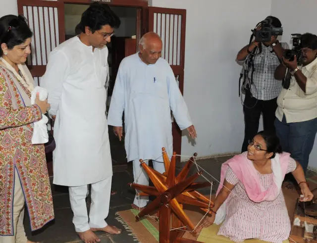 રાજ ઠાકરે અને અન્યો જેમાં એક મહિલા ચરખો કાતી રહી છે.