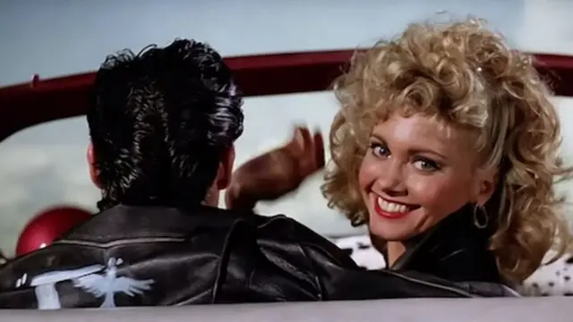 Frame da cena final do filme Grease, com Sandy (Olivia Newton-John) se despedindo olhando para a câmera