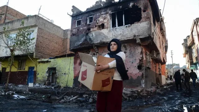 Diyarbakır'ın Sur ilçesinde 11 Aralık 2015'te çekilen bu fotoğrafta çatışmalarda yıkılan evlerde kurşun izleri görülüyor. Bir kadın da koli içindeki eşyalarını taşıyor.