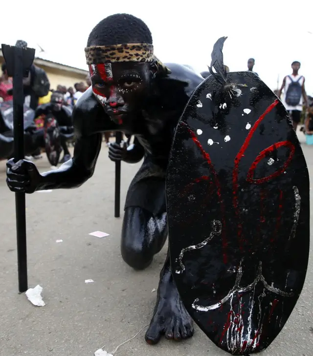 رجل مطلي باللون الأسود يجلس على الأرض، مع درع أسود ودعامة أخرى.