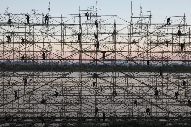 Men stand on scaffolding stand against a setting sun