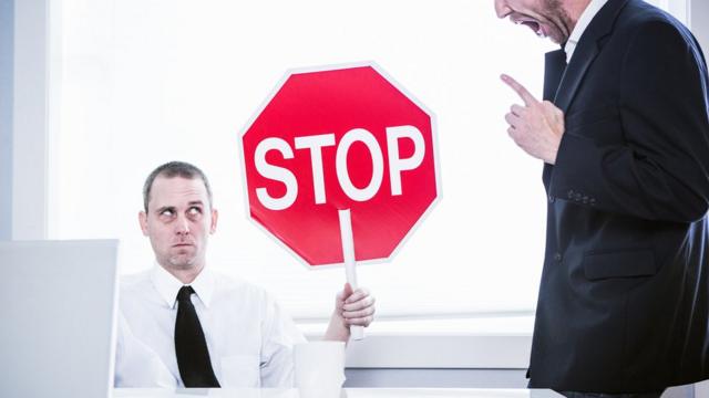 Trabajador con una señal de "Stop" ante un jefe abusivo.