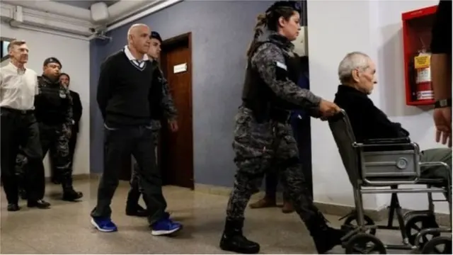 కోర్టు నుంచి వెళ్తున్న కొరాడీ(వీల్ చెయిర్లో వ్యక్తి), గోమెజ్(మధ్యలో), కొర్బాచో(ఎడమ వైపు)