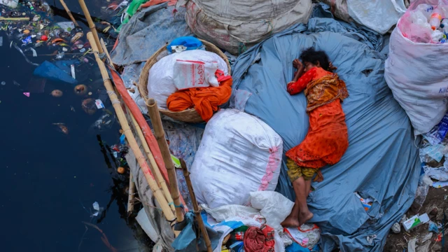 Mujer durmiendo a orillas de un río contaminado