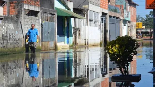 Homem usa galochasmines f12betborracha para atravessar rua inundada na periferiamines f12betSão Paulo