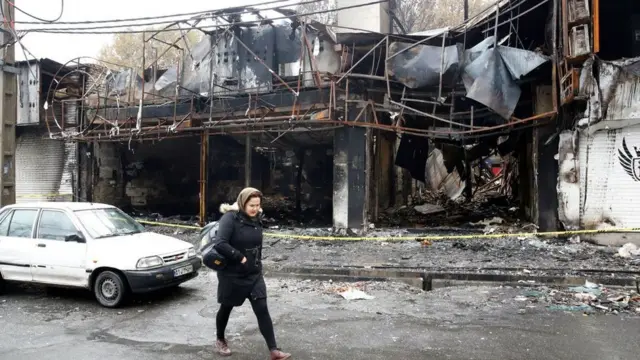 An Iranian woman walks past a shopping centre that was burned during protests over increasing fuel prices in the city of Shahriar, Alborz province, Iran, 20 November 2019.