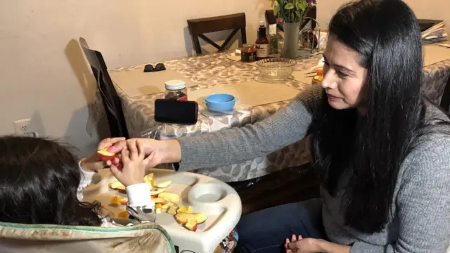 Uma mulher de cabelo preto dá frutas para uma criança