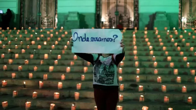 Em frente a escadaria com velas, manifestante segura cartaz que diz: 'Onde erramos?'