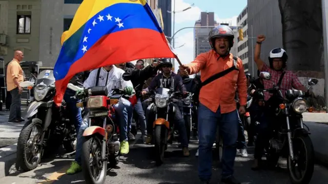 Motociclistas venezuelanos protestam em favor de Maduro; um deles está fora da moto, de pé, com uma bandeira do país